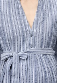 Κάθετο ριγέ φόρεμα μπλε και λευκό με δύο κουμπιά μπροστά και δέσιμο στη μέση σε ένα άτομο.