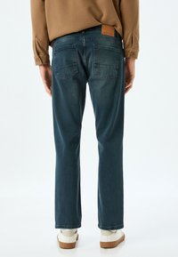 Tummansiniset farkut suoralinjaisella leikkauksella, joissa on kaksi takataskua ja nahkaleima vyötäröllä. Yhdistetty vaaleanharmaisiin lenkkareihin.