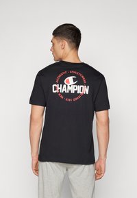 Sort bomulds t-shirt med et stort hvidt og rødt "Champion" logo på ryggen, rund design, korte ærmer og klassisk pasform.