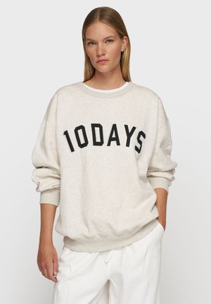 Lys beige sweatshirt lavet af blødt stof, med fed sort tekst der læser "10DAYS" på brystet. Løs pasform, ribbede manchetter og kant.