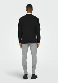 Schwarzes Sweatshirt mit langen Ärmeln, gerippten Bündchen und Saum. Kombiniert mit hellgrauen, taillierten Hosen und schwarzen Schuhen. Einfaches Design, keine sichtbaren Muster.
