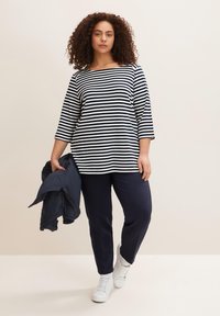 Gestreifte Bluse in Marineblau und Weiß, mit weitem Ausschnitt und Dreiviertelärmeln. Kombiniert mit Marineblauem Hosen und weißen Turnschuhen.