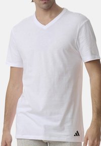 Biała bawełniana koszulka z dekoltem w serek i krótkimi rękawami; na dolnej lewej stronie znajduje się małe czarne logo Adidas. Miękka struktura.
