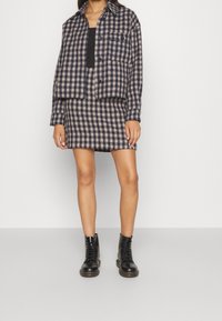 Conjunto de chaqueta y falda a cuadros en marino y beige. La chaqueta es corta, con un bolsillo abotonado, combinada con una falda ajustada y botas negras.
