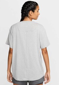 Top deportivo de manga corta en gris claro, con un escote redondeado, que presenta un detalle de costura en la parte posterior y un logo sutil en la parte superior de la espalda.