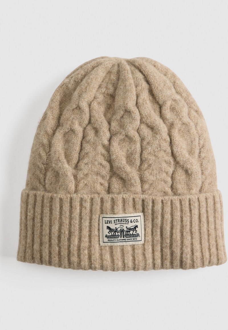 Beige Strickmütze mit geripptem Bündchen, ausgestattet mit einem Zopfmuster. Enthält ein rechteckiges Etikett mit dem Branding "Levi Strauss & Co.".