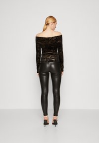 Top nero senza spalle con sottili scintillii metallici, abbinato a pantaloni di pelle nera lucida e sandali con tacco alto.
