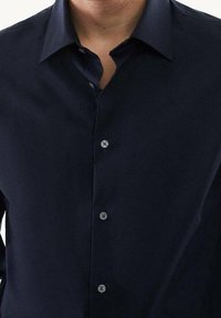 Chemise bleu marine à boutons pression, dotée d'un col classique et d'une texture lisse, avec six boutons sur le devant et sans motifs visibles.