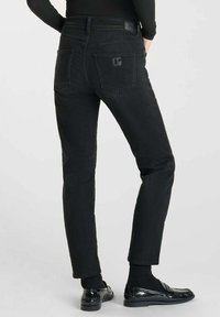 Jeans de mezclilla negra con un ajuste slim, que presentan un logo en el bolsillo trasero y costuras estándar. Textura suave y diseño clásico de cinco bolsillos.