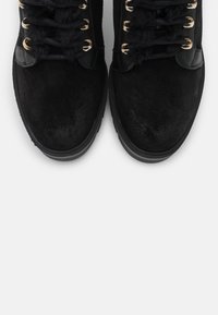 Černé semišové kotníkové boty s zlatými očky, černými tkaničkami a strukturovaným designem. Gumené podrážky zajišťují přilnavost a odolnost.