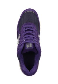 Zapatilla morada con parte superior texturizada, paneles de malla y cierre de cordones. Presenta un logo blanco y una suela de goma con puntera redondeada.