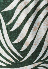 Zeleno blago z velikimi belimi in svetlo rožnatimi vzorci palmine listov ter teksturiranim ozadjem, ki ustvarja večplastni vizualni učinek.