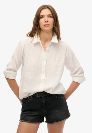 Witte linnen overhemd met een omgeslagen kraag, opgerolde mouwen, gecombineerd met zwarte denim shorts met een rafelige zoom.