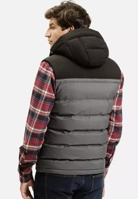 Kurtka puchowa ma czarny kaptur i szaro-skalistą sylwetkę z pikowaną teksturą; noszona na czerwonej koszuli w kratę. Design podkreśla ciepło i warstwowość.