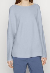 Pull en tricot bleu clair avec un col large, des manches longues et une coupe décontractée. Le tissu a une texture douce et un détail de côtes subtil.