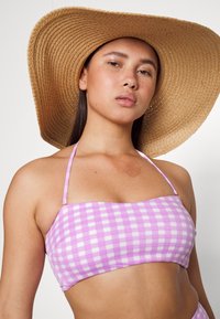 Top de bikini xadrez roxo e branco com decote reto e alças finas. Acompanhado de um chapéu de palha de abas largas. Textura suave.