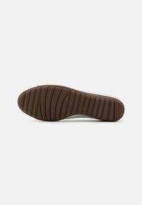 Semelle de chaussures avec un fond en caoutchouc marron, présentant des rainures horizontales et un dessus lisse, blanc. Aucun logo ou caractéristique supplémentaire visible.