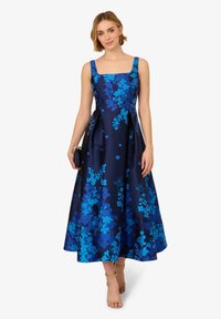 Blumenmusterkleid aus marineblauem Satin mit quadratischem Ausschnitt, breiten Trägern und einem ausgestellten Rock. Akzentuiert mit blauen Blumenmustern.