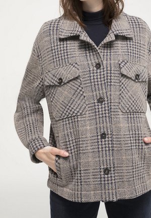 Chaqueta de cuadros de lana con grandes botones, bolsillos con solapa en el pecho y bolsillos laterales, llevada sobre un suéter de cuello alto negro.