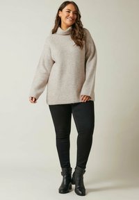 Maglione lavorato a maglia color beige chiaro con collo alto e maniche ampie, abbinato a jeans skinny neri e stivali neri alla caviglia. Morbido al tatto.