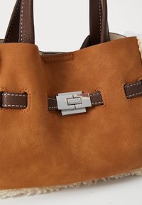 Sac en daim marron avec des poignées et une bandoulière en cuir marron foncé, fermoir rectangulaire en argent et bordure en fourrure crème au bas.