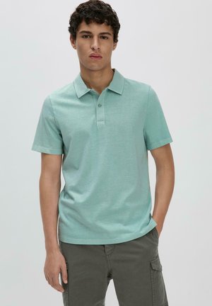 Hellgrünes kurzärmeliges Poloshirt aus einem weichen, strukturierten Stoff mit einer Drei-Knopf-Leiste und klassischem Kragen, kombiniert mit grauen Cargo-Shorts.