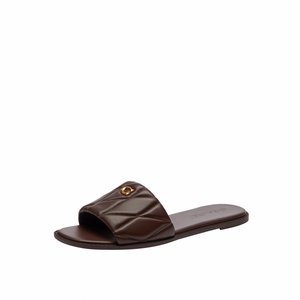 Sandalia tipo slide de cuero marrón oscuro con correa acolchada y pequeño emblema dorado en el lateral exterior, suela plana, diseño de puntera abierta.