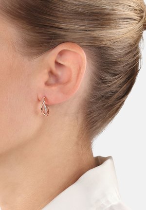 Rosenvergoldete Ohrringe mit Tropfendesign, das über filigrane Details und eine glatte Textur verfügt, getragen am Ohr eines Modells.