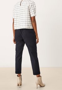 Bílý texturovaný top s námořnickou mřížkou, krátkými rukávy a detailem klíčové dírky na zádech, spojený s tmavě námořnickými zkrácenými kalhotami a béžovými kotníkovými botami.