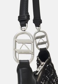 Sac à main en cuir noir avec un corps tissé texturé, quincaillerie en argent et accents de marque. Doté de doubles anses supérieures avec des clips décoratifs.