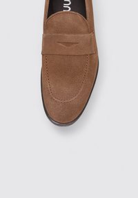 Mocassins en daim marron avec un capuchon de toe cousu et un détail de bande horizontale. Bout légèrement arrondi et semelle plate en caoutchouc pour le confort.