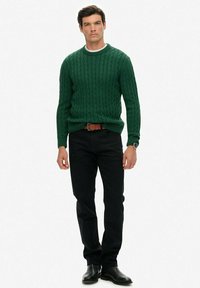 Groene kabelgebreide trui met een ronde hals, zwarte jeans en zwarte leren laarzen. De trui heeft geribbelde manchetten en een aansluitend ontwerp.