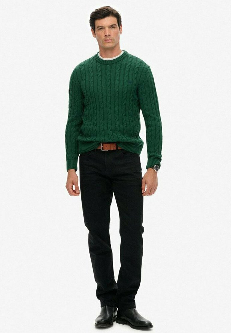 Groene kabelgebreide trui met een ronde hals, zwarte jeans en zwarte leren laarzen. De trui heeft geribbelde manchetten en een aansluitend ontwerp.