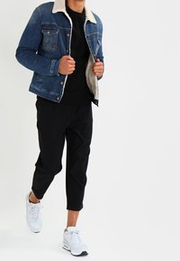 Jeansjacka med fårskinnskrage, ljusblå i färgen, i kombination med svarta cropped byxor och vita sneakers. Enkel, avslappnad design.