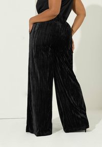 Zwarte wijde broek van fluweelachtige stof, met een verticale ribbeltextuur en zijzakken, voorzien van een elastische tailleband voor optimaal comfort.