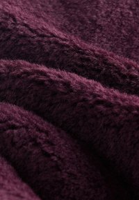 Pehmeä, pörröinen kangas syvän violetin värisenä, näkyvine kuituineen ja laskoksineen, jotka luovat teksturoitu, kodikas pinta.