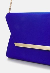 Clutch blu realizzato in tessuto liscio, con un accent gold rettangolare e una tracolla a catena. La borsa presenta una silhouette geometrica.