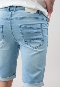 Bermudas de mezclilla azul claro con dobladillo enrollado, bolsillos traseros con acentos cosidos y una etiqueta cosida en la cintura.