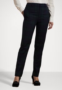 Pantalones a cuadros en verde oscuro y azul marino, fabricados con tejido tejido, de corte ajustado y textura suave. Combinados con zapatos de tacón alto negros.