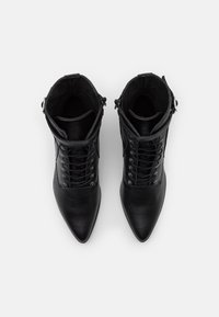 Botas de cuero negro hasta los tobillos con puntera afilada, que cuentan con un diseño de cordones, ojales plateados y cremallera lateral para facilitar su uso. Superficie texturizada.
