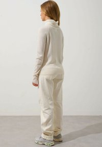 Krämfärgad polokrage-tröja med ribbade manchetter, tillsammans med krämfärgade vida byxor. Outfiten har mjuka, strukturerade tyger och en avslappnad passform.