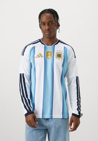 Camisa de futebol da Argentina de mangas longas apresentando listras verticais em azul claro e branco, logótipo da Adidas, emblema da FIFA e realces em azul-marinho.