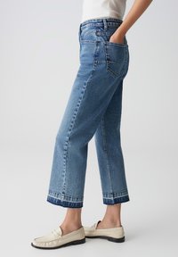 Jeans in denim azzurro chiaro con design a gamba dritta, orlo sfilacciato e due tasche posteriori. Indossati con mocassini crema.