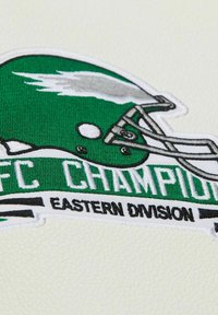 Toppa ricamata con un elmetto da football verde, testo "AFC CHAMPIONS" e "EASTERN DIVISION" in bianco e nero. Sfondo bianco con texture.