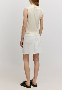 Lichtbeige mouwloze top met een ronde hals, gecombineerd met een witte denim minirok met een rafelrand en achterzakken. Zwarte slide sandalen.