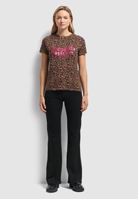 Koszulka w panterkę z różowym napisem "Francuska Muza". Krótkie rękawy, okrągły dekolt, w zestawie z czarnymi rozszerzanymi spodniami i czarnymi butami.