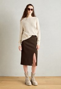 Suéter de punto acanalado en beige, falda midi acanalada marrón con abertura lateral y botas claras de cordones con suelas gruesas. Las gafas de sol añaden contraste.
