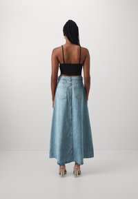 Lys blå denim maxiskjørt med høy midje, som har baklommer og en glatt finish. Kombinert med en svart, tettsittende topp med spaghetti stropper.