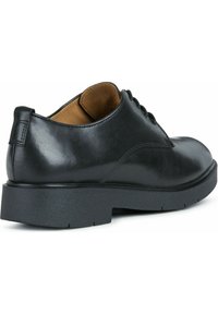 Scarpa nera in pelle con texture liscia, punta rotonda e suola in gomma bassa; presenta un design con lacci e un tacco piccolo.
