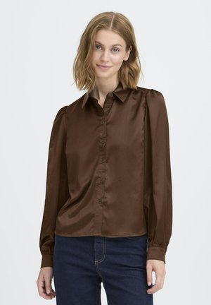 Braune Satin-Bluse mit langen Ärmeln, Knopfleiste vorn, spitzem Kragen und gerafften Schulterdetails. Kombiniert mit dunklen Denim-Jeans.